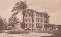 Douala, la Woermann-Line. – Cette compagnie de navigation allemande, dont on voit ici le siège au Cameroun, est issue du département de transport de la société de commerce fondée à Hambourg par Carl Woermann en 1837. Elle commence officiellement ses activités maritimes en 1885, au lendemain de la conférence de Berlin organisant le partage de l’Afrique entre puissances européennes, pour exploiter la desserte entre la métropole germanique et ses toutes nouvelles possessions du Cameroun, du Togo et d’Afrique orientale allemande (devenue Tanzanie, Rwanda et Burundi aujourd’hui). L’entreprise s’impose comme le principal opérateur sur ces destinations et ses représentations locales, à l’instar de celle de Douala, sont des lieux importants pour ces colonies dont l’économie est tournée vers l’extérieur. Elle développe une flotte moderne de paquebots mixtes, portent tous un prénom accolé au nom Woermann (Lucie Woermann, Ema Woermann, Adolf Woermann…). Après la première guerre mondiale, elle perd une partie de ses navires, saisis et partagés par les vainqueurs, mais poursuit ses activités africaines sous l’œil souvent suspicieux des nouveaux maitres du Togo et du Cameroun. Le romancier Jean Martet rapporte ainsi les propos recueillis en ce sens lors d’un voyage au Cameroun en 1933, reflétant la tension perceptible localement à l’égard des anciens adversaires: « A chaque fois qu’un bateau de la Woermann arrive à Douala, il donne une fête… [explique un commerçant français] […] Le représentant général de la Woermann s’appelle Firmenich. C’est un homme très gentil. Tous très gentils, je te dis. C’est un ancien commandant de bateau de guerre. Lui, il dit : de croiseur. Moi, je dis de sous marin. » (1). La compagnie maritime cessera finalement d'exsister durant la seconde guerre mondiale. La branche commerciale existe encore, mais elle a focalisé son action sur des marchés très porteurs et sans rapport avec l'histoire coloniale allemande, le Ghana, le Nigeria et l'Angola. Sources : (1) Martet, Jean, Les bâtisseurs de royaumes, Paris, Albin Michel, 1934.