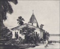 Akwa, le temple de Saker restauré, tel qu’il a subsisté jusqu’en 1945. – Le missionnaire baptiste britannique Alfred Saker est un pionnier à plusieurs titres : il fut l’un des tout premiers religieux à investir la côte que l’on nommait alors Cameroons, où il s’installa dès 1845, et il fut le premier à fabriquer des briques en terre cuite dans toute la région. En habile artisan, ce mécanicien-constructeur de marine parvint, à partir de 1860, à produire deux mille briques par semaine. Avec ce nouveau matériau, il put bâtir son temple, une école et une maison d’habitation. Ses constructions, sans briller par leur architecture, se démarquaient de l’existant où dominaient les matériaux d’origine végétale.  Le plateau d’Akwa, qui est aujourd’hui un quartier de Douala, est décrit en 1826 par un voyageur britannique comme propre, ordonné et structuré par deux vastes avenues parallèles, et surplombé par la vaste demeure à étage du roi. Quand Saker s’y installe, les rares autres constructions européennes sont des factoreries, dépôts fonctionnels destinés au commerce de traite. Il faut noter que les bâtiments érigés par Saker devaient s’avérer bien plus résistant que les premières constructions allemandes, souvent préfabriquées en bois et métal.