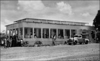 Foumban, le tribunal. – La ville de Foumban, capitale du royaume Bamoun, est le siège du pouvoir de cet empire parmi les plus anciens d’Afrique. Les autorités mandataires françaises (cette partie du Cameroun est placée en 1922 sous mandat français par la Société des Nations) vont s’employer à réduire l’emprise du sultan du Bamoun. Ainsi, Foumban devient une simple région dès 1922, puis l’année suivante une subdivision de la circonscription de Dschang. La même année, le souverain Njoya est déposé.  Exilé à Mantoun dans un premier temps,  puis à Yaoundé, il meurt en 1933, scellant la disparition de l’organisation politique Bamoun et la suprématie de l’administration française. L’affluence au tribunal, sur cette photo qui date des années 1950, en est le symbole.