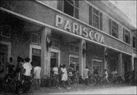 Douala, magasin Pariscoa (photo A. Gouelle).  – A la recherche d’une formule susceptible de rénover le commerce dans les capitales africaines, de type « grands magasins » et se démarquant des comptoirs, la SCOA (Société commerciale de l’Ouest Africain) s’associe à partir de 1952 avec le groupe Prisunic pour lancer une  chaîne de magasins sous l’enseigne Pariscoa et avec le groupe du Printemps pour ouvrir des magasins Printania. – « La clientèle européenne suffirait à elle seule à faire vivre un certain nombre de commerces (5 à 6000 Européens à Douala, sans compter les « broussards » qui viennent s’y ravitailler) ; la formule ancienne – comptoirs ou boutiques grecques – cherchant à convenir à la fois aux Européens et aux Africains, dont les goûts et les besoins sont souvent différents, semble condamnée à disparaître ». Source : « Douala, porte du Cameroun » (brochure), Douala, Secrétariat social du Cameroun et Chambre de commerce, d’agriculture et d’industrie du Cameroun, 1953.