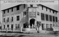 Duala, le Grand Hôtel. – Le Grand Hôtel est ouvert par un certain Millet, qui était arrivé en 1917 à Douala après s’être fâché avec son beau frère avec qui il devait exploiter le Grand Hôtel de Conakry. Il commença par un plus petit établissement, il n’avait que 2 francs et 25 centimes en caisse le jour de l’ouverture le 13 juillet 1917. Mais Douala foisonnait alors de soldats français, et plus encore de soldats anglais, qu’il fallait nourrir et abreuver. Millet gagna rapidement de quoi  s’agrandir et loua le Grand Hôtel. Mais c’était un homme changeant, et il se désintéressa vite de cette activité et se lança successivement dans le commerce du pain, avec l’idée de conquérir le marché indigène,  dans les transports en commun entre Douala et New-Bell, dans le transport de marchandises entre les quais et Douala, avec des tracteurs et des trains de remorques, dans l’approvisionnement de Douala en bois de chauffe, s’était en 1926, puis devint libraire… Source : Martet, Jean, Les bâtisseurs de royaumes, Paris, Albin Michel, 1934.