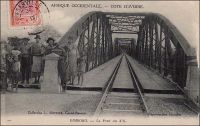 Dimbokro, le pont du N’zi. - Les travaux du chemin de fer « Abidjan-Niger » débutent en 1904. En 1909, le N’zi, une rivière, constitue la dernière grosse difficulté de la partie équatoriale du tracé ferroviaire ; il est franchi grâce à ce viaduc de 255 mètres de long. L’ouvrage et la gare de Dimbokro sont inaugurés le 11 septembre 1910, par le gouverneur général Angoulevant. La gare de Dimbokro reste le terminus du premier tronçon exploité, long de 181 km, jusqu’à l’ouverture en 1912 d’un nouveau tronçon de 135 km menant à Bouaké. Puis, entre 1919 et 1923, les 55 km séparant Bouaké de Katiola sont couverts. Entre 1924 et 1929 le tronçon Katiola-Ferkéssédougou, long de 187 km, est construit ; les 238 km supplémentaires, permettant de rallier Bobo-Dioulasso, sont achevés en 1932. La jonction ferroviaire entre Abidjan et Ouagadougou est réalisée en 1954. Enfin, du temps de la révolution Burkinabè (1983-1987), un réel effort populaire permet la construction d’un tronçon supplémentaire d’une centaine de kilomètres jusqu’à Kaya, à l’instigation de Thomas Sankara lui-même. Ce dernier tronçon n’a jamais été exploité. L’ambition était de joindre le gisement de manganèse de Tambao, à 200 km au nord de Kaya, sur lequel le pays fondait alors beaucoup d’espoirs.