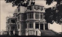 Abidjan, Hôtel du Gouvernement. – Ce palais rococo se dressait à l’emplacement de l’actuelle Présidence de la Côte d’Ivoire. Symbole du pouvoir colonial, il fut démoli après l’indépendance et remplacé par un bâtiment sans grand caractère. Sa construction avait été envisagée dès 1924, et pour la première fois on avait confié le projet à un cabinet d’architectes, Jaussely et Olivier qui était spécialisé dans l’architecture coloniale. Précédemment, la réalisation de tous les édifices officiels de Côte d’Ivoire était assurée par les Travaux Publics, un service de l’administration coloniale. Ce premier recours à une signature architecturale correspond à un revirement dans la politique antérieure du moins coûtant, tandis que cette colonie ne cesse de prospérer. Le chantier ne fut effectivement entamé qu’en 1931. Il avait finalement était confié à l’architecte Baudouin qui résidait à Abidjan. La construction, qui dura deux ans, ouvrait l’ère des grands travaux préparant le transfert de la capitale à Abidjan – elle se trouvait précédemment à Bingerville - en 1933. La richesse des décorations et installations du palais étaient alors inédite en Côte d’Ivoire.