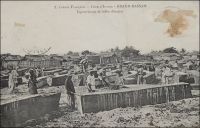 Grand-Bassam, équarrissage de billes d’Acajou. - « On parlait aujourd’hui des bois de la Côte d’Ivoire et l’on déplorait que les ébénistes français se servissent si peu des produits de nos colonies. Je citai Sue et Mare me disant que, quand ils avaient acheté en France une certaine qualité de bois exotiques, ils n’étaient jamais sûrs de retrouver ensuite la même, tant nos marchands en gros achètent à tort et à travers, au hasard des marchés. […] La baisse du franc du franc a mis nos acajous à des pris si peu élevés que plusieurs maisons américaines se sont installées à Grand-Bassam. Elles envoient nos bois précieux aux Etats-Unis d’où ils nous reviennent en France sous le nom d’acajou d’Amérique ». Source : Morand, Paul, A.O.F. de Paris à Tombouctou, Paris, Flammarion, 1928.