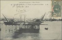 Grand-Bassam, le wharf, vue prise de la rade. – « Nous passons devant Grand-Lahoue : quelques factoreries établies entre la lagune et la mer. Grand-Bassam a cependant un wharf, qui permet de débarquer en évitant la barre ; on nous l’ouvre par faveur, car il n’est pas encore « reçu » par le service des Travaux publics (le lecteur voudra bien se souvenir que nous sommes en 1900) » (1). –  Ce premier wharf, long de 177 m, est inauguré en 1901. En 1923 l’adjonction, toujours à Grand-Bassam, d’un nouveau wharf de 288 m, permet d’accroître de 140 000 t. la capacité annuelle du trafic maritime. En 1931, , un nouveau wharf situé à Port-Bouët est mis en service pour décongestionner les installations de Grand-Bassam. Plus proche d’Abidjan, celui-ci est supposé inciter les entreprises à se rapprocher de la capitale, dans laquelle le percement d’un canal entre océan et lagune doit permettre d’installer un port eau profonde. Le projet, qui remonte au début du XXème siècle et avait été abandonné au moment de la première guerre mondiale, voit finalement le jour avec l’ouverture du canal de Vridi en 1951, scellant l’abandon des wharfs. Source : (1) Gouraud, Gal, Zinder Tchad, Paris, Plon, 1944.