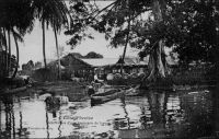 Débarcadère d’une factorerie de lagune. – Le commerce de traite, qui prévaut dans le système colonial, consiste à échanger des marchandises manufacturées occidentales contre des matières premières tropicales, lesquelles sont ensuite revendues sur le marché métropolitain. Selon les époques et les lieux, ces échanges utilisent la monnaie, ou s’en affranchissent. La factorerie est la base locale de ce négoce. La première factorerie de Côte d’Ivoire aurait été créée en 1863 par le rochelais Arthur Verdier, à Assinie, où résidait alors le représentant de la France. Le peu d’empressement des grandes compagnies commerciales à développer leur réseau en Côte d’Ivoire, laissa la place à de petits commerçants qui maillèrent progressivement le territoire. A partir de 1858, les négociants étrangers furent d’ailleurs autorisés à s’installer dans les comptoirs français. La factorerie à proprement parler (on ne voit ici que le débarcadère) n’est bâtie en dur que lorsqu’elle s’est avérée viable commercialement, disposant d’un réseau de sous-factoreries dans l’intérieur du pays. La construction comprend alors un solide rez-de-chaussée, pour protéger le stock, aux épais murs de maçonnerie de pierre ou de briques importées, et avec de petites ouvertures à barreaux. L’habitation du traitant est aménagée à l’étage, dans un bâti plus léger, et entourée d’une galerie.