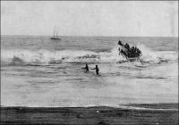 Grand-Bassam, le surf-boat a bondi au sommet de la barre. – Le débarquement acrobatique sur les côtes du golf de Guinée tel qu’il avait lieu avant la construction des wharfs. Le voilier que l’on aperçoit au second plan de l’image, est une  goélette qui servait de « salle d’attente » aux voyageurs arrivant. Déposés là par les paquebots, ils pouvaient avoir à passer plusieurs jours à bord, avant que ne se présente le moment propice pour franchir la barre. Le wharf de Grand-Bassam fut construit en 1897. La photo et le récit qui suit sont donc antérieurs. « Il y a trois jours, le paquebot venant de Marseille mouillait devant Grand-Bassam ; je m’imaginais être au terme de mes tribulations sur mer, je m’apprêtais à débarquer… une surprise m’attendait. D’un ton légèrement narquois le commandant du bord m’annonça que la barre était infranchissable… Jusqu’ici ne n’avais vu de barre qu’à l’embouchure des rivières. Dans le golfe de Guinée le phénomène se produit sur toute la côte et est dû à une disposition particulière du littoral. […] Ici la pente de la plage est très rapide : les lames qui s’y précipitent rencontrent presque un à-pic, et leur pied heurtent un obstacle, elles s’écoulent sur elles-mêmes, sapées dans leur base, cataractes et tourbillons qui écrasent sous leur masse et rejettent brisées à terre les barques assez téméraires pour vouloir passer. C’est la barre. […] Seul un wharf pourrait dompter les flots et s’avancer, victorieux, au-devant des paquebots ; mais à Grand-Bassam le wharf est encore à l’état de projet. Que deviennent les donc les passagers lorsque la barre est impraticable et que nulle embarcation n’ose l’affronter ? L’administration, toujours prévoyante, a résolu ce problème : en rade se balance une vieille goélette solidement ancrée au milieu des vagues, sorte de ponton qui assure un asile aux voyageurs en détresse. Trois matelots nègres et un patron également noir ont la garde du bord.» témoignage rapporté par le colonel Baratier (1). Source (1) Baratier, Col., A travers l’Afrique, Paris, Arthème Fayard, 1908.