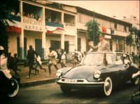 Le convoi du Général De Gaulle dans les rues de Conakry, le 25 août 1958 (cliché amateur de Léon Anselmo). – A la veille du référendum du 28 septembre 1958, le Général De Gaulle fait la tournée des capitales africaines. Il s’emploie à  convaincre les populations de voter en faveur de l’adhésion de leur territoire respectif à la Communauté française. Ce nouveau statut, qui confère aux colonies une grande autonomie, fait partie du projet de constitution de la Vème république. L’accueil du nouveau chef de l’exécutif français – il est revenu au pouvoir depuis quelques mois seulement, porté par les difficultés de la décolonisation algérienne – est contrasté. A Conakry, il est chaleureusement fêté, la population est mobilisée pour saluer son passage et Ahmed Sékou Touré est venu en personne le chercher à l’aéroport (on l’aperçoit d’ailleurs dans la voiture aux côtés du général) alors qu’à l’étape suivante de Dakar ni Léopold Sédar Senghor ni Mamadou Dia, le président du gouvernement du Sénégal, ne seront là. Mais bien vite c’est le malentendu : le discours du leader guinéen est une douche froide pour l’homme du 18 juin. Il clame préférer « la pauvreté dans la liberté, à la richesse dans l’esclavage » et appelle son peuple à refuser la Communauté pour choisir l’indépendance. Le Général De Gaulle est ulcéré, il prend acte sèchement en parlant de « sécession » et quitte Conakry très contrarié. Lors du référendum, le oui l’emporte largement dans toutes l’Afrique (y compris au Niger où l’administration a falsifié les résultats semble-t-il) sauf en Guinée qui accède à l’indépendance dès le 3 octobre. Et le torchon continue de bruler entre Conakry et Paris, puisque la passation de pouvoir prend la forme d’une rupture économique et politique brutale. Malgré les tentatives de réconciliations tentées par Sékou Touré, De Gaulle et Jacques Foccart - son homme de l’ombre en charge des affaires africaines – lui en tiendront rigueur jusqu’au bout, multipliant même les tentatives d’attentat à son égard.