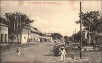 Conakry, rue commerciale. - Connue également comme avenue commerciale, rue, avenue ou boulevard du Commerce ou encore « 3ème boulevard », cette artère majeure de la capitale guinéenne aboutit au port. L’administrateur Bie la décrit ainsi en 1899 : « n’a pas moins de 30 m. de large sur une longueur d’environ un kilomètre. De larges trottoirs bordant cette rue, de splendides maison à étage, toutes neuves, lui donnent une apparence toute moderne » (1). Le chemin de fer Decauville, que l’on distingue sur l’image, fut déployé dans ce quartier de négoce à partir de 1897. Cette installation, constituée de rails écartés de 60 cm et fixés sur des traverses métalliques, était souvent désignée comme « petite vitesse », par opposition au chemin de fer plus rapide et en voies métriques qui joignait le fleuve Niger. A partir de 1902, elle totalisait 9,7 kilomètres de voies. Son usage n’était pas réservé au commerce, et les particuliers pouvaient y faire circuler des marchandises, moyennant un droit de 1 franc par tonne transportée et en fournissant le véhicule et son mode de traction. Les wagonnets de promenade, emportant des passagers, n’étaient pas soumis à cette taxe. Source (1) : Bie. A. (administrateur), Voyage à la côte occidentale d’Afrique, de Marseille à Conakry, Conakry le 20 mai 1899 (archive privée citée par Odile Goerg dans Rives Coloniales, Soulilou, Jacques, éditeur scientifique, Paris, édition Parenthèses et édition Orstom, 1993).