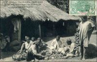 Haute-Guinée, achat du caoutchouc en factorerie. Coupage des boules. – Cette opération vise à contrôler la qualité du produit récolté, car la fraude était répandue dans le commerce guinéen du caoutchouc : les boules contenaient jusqu’à 25 % d’impuretés, comme des cailloux, pour en augmenter le poids. La demande de caoutchouc, engendrée par le développement de la bicyclette et de l’automobile à la fin du XIXème siècle, stimule la production en Guinée, alors appelée les Rivières du Sud. Contrairement à l’Amazonie où l’on tire la matière première des hévéas, on exploite en Guinée des lianes à latex. Le produit obtenu est de piètre qualité, les rendements sont faibles, mais l’affaire est rentable pour les traitants dans la mesure où la main d’œuvre est contrainte par la nécessité d’acquitter l’impôt colonial. La « ruée sur le caoutchouc » a de fortes conséquences sur la trajectoire économique et sociale du pays. Le travail nécessaire à la récolte et au transport du latex, tandis qu’il faut toujours aller le chercher plus loin, mobilisent les populations, au détriment de toutes les autres cultures, y compris vivrières. A l’époque où fut prise cette photo - vers 1905 quand le photographe Fortier se rendit en Haute-Guinée par le fleuve Niger-, la Guinée exportait près de 1700 tonnes de caoutchouc par an ; soit les deux tiers des exportations guinéennes en valeur. Quand les plantations d’hévéa d’Extrême-Orient entrèrent en production vers 1910, le produit guinéen, cher et médiocre, se trouva totalement disqualifié. La crise qui s’en suivit fut très dure, et dura jusqu’à ce que les exportations de banane aient remplacé celles de caoutchouc. L’économie de la Guinée a connu quatre cycles successifs durant les deux derniers siècles : les esclaves, le caoutchouc, la banane et la bauxite.