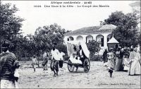 Une noce à la Côte. Le coupé des mariés. – La Guinée maritime était occupée, encore au XIXème siècle, par des populations peu évoluées et peu islamisées. L’influence économique et sociale du commerce maritime européen, remontant pourtant au XVème siècle, était restreinte à quelques clans privilégiés qui contrôlaient les comptoirs et leurs abords. Longtemps, ces derniers contribuèrent au désordre persistant dans la région, en se livrant à de perpétuelles rivalités armées, souvent suscitées par les commerçants européens concurrents. Cette insécurité persistante n’étant pas favorable au commerce conventionnel, c’est principalement la traite d’esclaves qui se développa. Si une grande partie de la population des « Rivières » restait en marge de ce commerce, il émergea néanmoins au XIXème siècle une bourgeoisie fortunée de commerçants et de planteurs esclavagistes, mêlant les descendants métis de traitants américains, portugais ou français à des éléments de la chefferie locale, et vivant matériellement à l’européenne. L’implantation de sociétés commerciales européennes dès le début du XXème siècle, favorisée par l’administration coloniale, devait disqualifier cette élite économique locale, la ramenant au rang de notables. Cette bourgeoisie d’ancienne origine devait renaître en partie, juste après la seconde guerre mondiale, à la faveur du développement de la culture bananière (1). - Cette carte fait partie du travail du célèbre photographe et éditeur dakarois Edmond Fortier (1862-1928) à qui l’on doit une somme importante de clichés sur toute l’Afrique de l’Ouest. M. Fortier tenait boutique non loin du marché Kermel, à l’angle de la rue Dagorne et du boulevard Pinet-Laprade. Cette photo doit dater de 1902-1903. Edmond Fortier a en effet effectué deux voyages en Guinée ; l’un en Guinée maritime en 1902 ou 1903 à partir de Conakry, et l’autre en Haute-Guinée, en 1905, en passant par le fleuve Niger et son affluent le Milo depuis Bamako à l’occasion d’un périple au Soudan français, comme cela se faisait avant l’arrivée du chemin de fer. Sources : Suret-Canale, Jean, La République de Guinée, Paris, Editions Sociales, 1970.