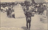 Bobo-Dioulasso, le marché. –En mars 1890, le commandant Monteil fait étape à Bobo-Dioulasso, durant sa fameuse expédition de Saint-Louis du Sénégal à Tripoli en passant par le Lac Tchad. Il décrit le marché et ses échanges en ces termes : « Bobo-Dioulasso est un marché important où se tissent des cotonnades célèbres d’une grande finesse de trame en même temps que de grande solidité. Les principales transactions du marché portent sur l’or, la noix de kola et le coton. La noix de kola vient du sud du Ouorodougou et de Gondia ». Pour l’explorateur, le séjour dans cette ville voltaïque réserve quelques déconvenues. Il y est abandonné par la fuite de ses porteurs. Outre ces derniers, il voyage avec une troupe légère, composée d’un adjudant français et de douze tirailleurs sénégalais. Il soupçonne son cuisinier d’être l’organisateur de cette défection. Mais celui disparait à son tour, avant de reparaitre à Ségou, où il raconte une histoire confuse aux autorités militaires françaises, évoquant le massacre par des brigands de toute la mission Monteil, dont il serait le seul survivant. Mais son affabulation ne convainc pas et il est décapité pour désertion. Monteil, qui relate cet épisode, prit connaissance de son issue après son retour en France. Réputé esprit audacieux – il prédit même l’indépendance de l’Indochine dans ses écrits dès le début du XXème siècle -, il ne parait pourtant pas choqué ou même affecté par la sévérité de la sanction pour une faute si vénielle… Cette photographie, localisée au Haut-Sénégal-Niger, se situe chronologiquement entre 1904, création de ce territoire, et 1919, naissance de la colonie de Haute-Volta.