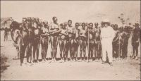 Chez les Lobis, le coin des « Yona », femmes. – La rencontre avec la nudité – partielle ou totale - de certains groupes africains surprend les occidentaux de la fin du XIXème et du début du XXème siècle. Particulièrement celle des femmes, qui n’est pas coutumière dans l’Europe d’alors. Les témoignages sur le sujet, écrits ou photographiques, sont nombreux. Ils mettent parfois en scène, comme ici, une représentation étrange à force de contrastes, où le colonisateur se montre très habillé aux côtés d’Africains dévêtus. Ce genre de tableau semble à la fois flatter le gout de l’exotisme des visiteurs et justifier implicitement l’ambition civilisatrice –au sens normatif- de l’action coloniale… L’écrivain Jacques Soubrier, auteur de romans pour les jeunes et de récits voyages, raconte ainsi sa rencontre avec les tribus Lobis les jours de marché à Gaoua lors d’un périple africain : « Les femmes n’ont pour tout costume que la ceinture de ficelles, en brin de « bemwos », dont les extrémités leur pendent jusqu’aux genoux. Les femmes mariées portent, en outre, comme chez les Bobos, deux bouquets de feuilles, qu’elles s’appliquent avec beaucoup de pudeur lorsqu’elles se baissent. La plupart ont les lèvres déformées par l’affreux labret de quartz, de fer, d’os ou de bois, et des scarifications en étoile leur ornent le nombril. Leurs traits sont en général assez fins et l’habitude, commune à toutes les femmes noires, de porter les fardeaux sur la tête donne à leur démarche et à leur port l’élégance et la noblesse que l’on remarque, pour la même raison, chez nos Arlésiennes » (1). Carte postale signée « Cliché Mission d’Art Colonial ». Source : Soubrier, Jacques, Savanes et Forêts, Paris, J. Susse, 1944.