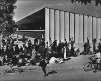 Ouagadougou, le marché, vers 1950. – Il s’agit du marché central Rood Woko, peu après sa construction. Le nom Rood Woko est composé de deux mots qui signifient respectivement en mooré « fréquenter » et « long », lesquels, mis ensemble, évoquent un marché animé quotidiennement, par opposition à d’autres qui sont périodiques. Agrandi et modernisé en 1983, ce marché a été partiellement détruit dans un incendie le 27 mai 2003, et fermé. Officiellement, le sinistre est imputé à un court-circuit, mais le marché se situe dans une zone qui était alors en cours de démolition, dans le cadre de l’opération « Zaka » destinée à créer un centre ville « moderne » après avoir déplacé les anciens occupants vers la grande périphérie de la capitale… Après des années atermoiements, d’annonces contradictoires, et de tensions parfois violentes entre autorités municipales et commerçants, les travaux de réhabilitation de l’édifice ont débuté le 27 août 2007, 51 mois jour pour jour après l’incendie.