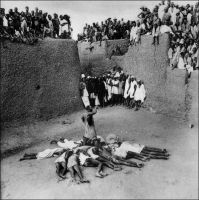 Enterrement en pays Bobo, vers 1930. – « Mon séjour en pays Bobo me donne l’occasion d’assister à un enterrement fétichiste. La cérémonie se déroule sur une place entourée par les hautes murailles fauves des maisons sans fenêtres. Une multitude frémissante de boubous blancs garnit les terrasses, déborde sur les moindres saillies, les plus petits pans de mur. […] Six noirs surgissent en courant, portant sur leurs épaules, enveloppé dans une natte, un long paquet qu’ils déposent à terre aussitôt. […] Les masques font leur entrée, couverts de vêtements en fibres rouges et brunes qui leur cachent entièrement le corps. […] Puis un féticheur s’avance pompeusement, pénétré de l’importance de ses fonctions, la tête couverte d’une toile, et portant une idole informe, en bois garni de plumes ; il enjambe le mort, lui met la statuette sous le nez à plusieurs reprises, et s’accroupit sur lui sans façon, comme s’il voulait en éprouver l’élasticité, faisant à chaque fois sursauter le cadavre. […] On enferme à nouveau le cadavre dans sa natte, et une douzaine de parents s’allongent sur le ventre, en étoile, posant chacun leur tête sur le cadavre. […] Un autre individu entre en scène […] faisant tournoyer au dessus de sa tête un fer de lance retenu par une corde […] laisse filer petit à petit toute la corde obligeant l’assistance à se reculer au maximum […] La foule se referme à nouveau et jette des cauris, accompagnant de ses clameurs le départ du cadavre que l’on enlève au pas de course […] Les morts vont vite, à Bobo ! Les morts vont vite, à Bobo ! ». Source : J. Soubrier, Savanes et forêts, éditions J. Susse, Paris, 1944.
