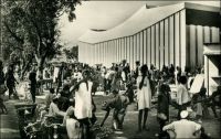 Ouagadougou, le marché, vers 1950. – Il s’agit du marché central Rood Woko, peu après sa construction. Le nom Rood Woko est composé de deux  mots qui signifient respectivement en mooré « fréquenter » et « long », lesquels, mis ensemble, évoquent un marché animé quotidiennement, par opposition à d’autres qui sont périodiques. Agrandi et modernisé en 1983, ce marché a été partiellement détruit dans un incendie le 27 mai 2003, et fermé. Officiellement, le sinistre est imputé à un court-circuit, mais le marché se situe dans une zone qui était alors en cours de démolition, dans le cadre de l’opération « Zaka » destinée à créer un centre ville « moderne » après avoir déplacé les anciens occupants vers la grande périphérie de la capitale… Après des années atermoiements, d’annonces contradictoires, et de tensions parfois violentes entre autorités municipales et commerçants, les travaux de réhabilitation de l’édifice ont débuté le 27 août 2007, 51 mois jour pour jour après l’incendie.