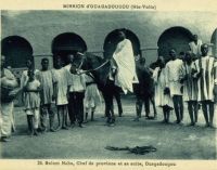 Morom Naba, chef de province et sa suite, Ouagadougou – Carte postale éditée par la Mission de Ouagadougou – Il doit s’agir du Mogho Naaba Koom (1889 – 1942), l'arrière grand-père du Mogho Naaba actuel, un empereur qui avait choisi pour devise «Que l'eau abonde pour tous». Mogho Naaba Koom s’était rallié à la France Libre dès le 22 juin 1940. Il repose, ainsi que sa femme, au centre de la place qui porte son nom, devant la gare ferroviaire de Ouagadougou, sous la masse d'une statue métallique de 6 mètres de haut représentant une femme mossi stylisée offrant l'eau de bienvenue à un hôte invisible.