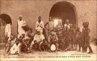 Un campement de la ligne d’étape Kano Zinder. - Distantes de 250 km, les villes de Zinder au Niger et Kano au Nigeria sont des escales importantes d’une voie de communication ancestrale, joignant le Golf de Guinée à l’Afrique du Nord, soit l’Atlantique à la Méditerranée via le Sahara. De longue date, des caravanes l’empruntent pour assurer les échanges entre les régions riches en or et ivoire et la tripolitaine. La conquête coloniale laisse une large partie du trajet dans le giron français, hormis l’extrémité méridionale, sous contrôle britannique. Même si elle est peu utilisée par les colonisateurs, qui préfèrent évoluer dans les limites de leurs propres possessions, elle reste néanmoins sécurisée par leurs soins, pour maintenir le commerce africain, source de revenus imposables. Pour cela, les étapes sont généralement érigées en postes militaires, gardés par une troupe indigène sous le commandement d’un officier ou d’un sous-officier européen. Cette piste n’est que rarement employée pour l’approvisionnement et le courrier des postes français du Niger, de la côte atlantique vers le sahel. Les voies via Say au Dahomey, voire via le Congo et le Tchad, lui sont préférées. Plus tard, après la Seconde Guerre mondiale, la ligne est exploitée par les petits autocars d’une entreprise privée algérienne. La Société des transports tropicaux relie ainsi le Maghreb à l’Afrique de l’Ouest, d’Alger à Kano en passant par Zinder, soit 3945 kilomètres, en 12 jours et 8 nuits d’hôtel passées dans les villes étapes. A Zinder, le voyageur venu d’Algérie pouvait aussi attraper –ou attendre- une correspondance pour Niamey ou Fort-Lamy.