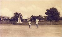 Fort-Lamy,  Place de la Libération et Monument aux Morts. – « L’entrée dans la ville est beaucoup plus décevante. Les concessions européennes sont minuscules, les jardins rares et pauvres, les arbres sur le bord du fleuve, les maisons ont un aspect sale et ruiné en raison de leur bâtisse de brique mauvaise que le soleil délite et de leur chaux locale, que la pluie délave. La place centrale est une sorte de désert où les enfants jouent au ballon, dans la poussière, les Européens au tennis ; les bicyclettes et les autos vont en tous sens et le marché indigène déploie ses paillotes, son odeur, ses incendies. […] Cette cité n’avait point d’ancêtre indigène. Fort-Lamy a été créé de toutes pièces après la victoire de Gentil sur Rabah. Les monuments de Gentil et Lamy, petits obélisques blancs entourés d’agaves ornent, si l’on peut dire, l’un la place, l’autre l’avenue du fleuve ». Source : Lapie, Pierre Olivier, Mes tournées au Tchad, Londres, John Murray, 1941.