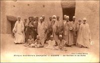 Zinder, le sultan et sa suite. – « Ahmidou, le sultan de Zinder, est un jeune homme [...]. Il est sous l’influence, probablement mauvaise, du premier ministre, qui porte le titre de Bellama. Il est beaucoup plus question dans Zinder de ce dernier que du sultan, qui fait cependant ce qu’il peut pour établir son prestige. [...] A Zinder, les habitants, en guise d’hommage et de remerciement, se mettent à genoux [à la vue du sultan] et se versent sur la tête des poignées de terre et de poussière. Seules les femmes sont dispensées de cette coutume. [...] La cour est importante ; elle se compose, après le Béllama, de plusieurs ministres ; l’un d’eux, le serky N’Touraoua est chargé des intérêts des blancs, c’est-à-dire des Arabes [...] Tout ce personnel, comme le sultan lui-même, est revêtu de plusieurs vêtements superposés qui leur donne l’air d’épais mannequins, coiffés d’un énorme turban » (1). – La carte représente peut être le personnage évoqué par Gouraud dans ses mémoires, ou l’un de ses successeurs. Le militaire avait été en poste à Zinder à compter de 1902, et la photographie signée « Photo Combier Mâcon »  fait partie des collections de la maison CIM (Combier imprimeurs à Mâcon) dont les activités s’étendent de 1907 à 1982. Fondée par Jean Combier, l’entreprise édita quelques 2 millions de carte postales essentiellement consacrées aux régions françaises – colonies comprises (2). Source : (1) Gouraud, Général, Zinder, Tchad - Souvenirs d'un Africain, Paris, Plon, 1944. (2) Combier, Marc, Un siècle de cartes postales, Paris, Alternatives, 2005.
