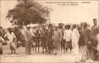 Zinder, un coin du marché. – Le général Gouraud, figure de la conquête coloniale, décrit ainsi Zinder et son marché en avril 1902 – il était alors commandant -, tandis qu’il y rentre pour la première fois : « Zinder est le grand centre de transit de cette partie de l’Afrique centrale. […] Au Nord, à 1500 mètres [de Zinder], se trouve la ville Targuie de Zengou. […] On y rencontre des Tripolitains, quelques Touareg. Elle compte 4 à 5000 habitants. […] Le marché de Zengou est animé. On y trouve en particulier de beaux cuirs, les bottes en filali de toute l’Afrique centrale et que nous portons nous-mêmes, des brides brodées ; les bijoux ne valent pas les délicats filigranes des bijoux soudanais et sénégalais ; il y a de jolies calebasses ouvragées de toutes dimensions, la calebasse pouvant servir d’écuelle aussi bien que de malle aux femmes du pays, qui y empilent leurs étoffes et leurs ustensiles et la portent sur la tête. On y voit des musiciens, des danseuses, aux cadences lentes et balancées, un homme-orchestre. Il y a encore sur le marché de Zengou du sel de Bilma, comme à Tombouctou du sel de Taodénit ». Source : Gouraud, Général, Zinder, Tchad - Souvenirs d'un Africain, Paris, Plon, 1944.