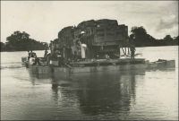 Passage d’un bac. – « Lorsqu’on arrive à Fort-Lamy par le fleuve, on voit une ligne d’arbres vert sombre, dominés du drapeau français, ponctuée de flamboyants et cachant des maisons blanches. A cet endroit la rive du fleuve, aux basses eaux, est élevée comme une falaise. On croit à un paradis de verdure à l’abri des eaux. Avant ce promontoire de feuilles, la rive s’est abaissée en pente douce et sableuse ; les pirogues chargées de poissons, de bois, de paille, d’hommes, de femmes, d’enfants, d’animaux, de calebasses ; ouvertes de frêles, lourdes et couvertes de shimbecks de paille, grées de filets immenses et des apparaux de la pêche, ou nues ; de baleinières de métal, poussées par des perches ; un bac transportant un camion, c’est le port. » Source : Lapie, Pierre Olivier, Mes tournées au Tchad, Londres, John Murray, 1941.