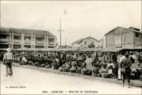 Dakar, le marché Sandyaga. - Construit entre 1933 et 1935, le marché Sandaga quelques fois orthographié « Sandyaga » comme ici ou « Sandiaga » - tiendrait son nom d’un arbre, « dang ga », marquant à l’époque son centre. Ce marché répond à une logique d’organisation ségréguée de la ville coloniale, progressivement instaurée dans la capitale sénégalaise depuis sa création dans la seconde moitié du XIXème siècle. Comme le note la légende manuscrite de l’auteur de cette photo, il est dévolu aux échanges des indigènes, et est situé le long d’axes menant aux quartiers périphériques où ils sont relégués. Sandaga approvisionne des marchés secondaires, formels et informels, situés dans les faubourgs populaires de la Médina. Les Européens, qui habitent dans le quartier du Plateau -agréablement tempéré par le vent du large-, vont au marché Kermel. Dans les rues autour de Sandaga se développe rapidement une zone commerciale très dynamique. Elle était tenue, jusque récemment, par de si nombreux marchands libanais qu’on désignait parfois Dakar sous le nom de « Beyrouth 2 ». Ils semblent avoir cédé la place à des commerçants sénégalais appartenant à la confrérie mouride. Sources : Sinou, Alain, Rives Coloniales, Paris, éditions Parenthèses et éditions de l’Orstom, 1993.
