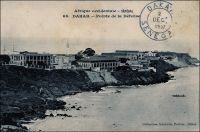 Dakar, Pointe de la Défense. – « Sur la falaise les quartiers militaires, près de leurs batteries, doivent aux nécessités tactiques la priorité des brises. Ces batteries furent construites aux mauvaises heures de Fachoda. Qui, alors, eut pensé que si elles devaient tonner un jour contre les vaisseaux de Sa Majesté, ce serait en 1940, après trente années d’amitié avec le peuple anglais !... Ce quartier militaire est aimable dans sa demi-désuétude. Le général commandant supérieur, ses états-majors et services, y travaillent à l’ombre, dans des hôtels et pavillons dont type série se retrouve dans toutes nos colonies. Des arbres très exotiques, baobabs, saucissonniers flamboyants, enveloppent les galeries blanches et les vérandahs à volets gris. Quelques rudes conquérants, qui fermèrent le livre de l’épopée soudanienne, sont passés ici. Sur le pavillon du chef d’état-major une plaque commémore le souvenir de Mangin. Le compagnon de Marchand fut sous-chef au Commandement supérieur, de 1906 à 1908 » (1). Cette carte postale fait partie du travail du photographe et éditeur dakarois Edmond Fortier (1862-1928). On lui doit une somme importante de clichés sur l’Afrique de l’Ouest en général et sur le Sénégal en particulier ; il a publié en tout 3300 prises de vue originales. M. Fortier tenait boutique et vivait avec ses deux filles blondes et son boy Seydou Traoré, à l’angle de la rue Dagorne et du boulevard Pinet-Laprade, tout près du marché Kermel. Sources : (1) Vanlande, René, Dakar !, Paris, Editions J. Peyronnet et Cie, 1945(?).