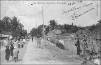 Saint-Louis, route de Sor. – L’île de Sor, située en face de l’île portant le centre ville de Saint-Louis, commence à se développer au XIXème siècle, à mesure que ses marécages sont assainis. Son aménagement, pour en faire une ville jumelle de Saint-Louis sous le nom de Saint-Philippe, avait été envisagé dès 1837 par le ministre de la Marine et des colonies de Louis-Philippe. Le projet, qui avait fait long feu, est relancé en 1852, et l’on baptise alors le nouveau quartier, implanté au nord de la vaste île, Bouetville en référence au gouverneur Bouet-Willaumet (1843-1845). Mais le lieu, isolé du centre par le grand bras du fleuve Sénégal, n’attire pas encore beaucoup d’habitants ; il n’en compte que 308 en 1857. La mise en place d’un bac régulier en 1858, puis d’un pont en 1865 par Faidherbe, facilite l’implantation humaine. L’arrivée du chemin de fer en 1885, dont l’ensemble des installations saint-louisiennes est déployé à Sor, va contribuer au développement du sud de l’île, baptisé Léona. Progressivement, les quartiers et les sous quartiers de Sor se structurent et se peuplent, dans un environnement luxuriant de cocotiers, de filaos et de prosopis verts. Au moment où le Sénégal accède à l’indépendance, en 1960, Sor compte 24 352 habitants.– Cette photo fait partie du travail du célèbre photographe et éditeur dakarois Edmond Fortier (1862-1928) à qui l’on doit une somme importante de clichés sur l’Afrique de l’Ouest en général et sur le Sénégal en particulier ; il a publié en tout 3300 clichés originaux. M. Fortier tenait boutique et vivait avec ses deux filles blondes et son boy Seydou Traoré, à l’angle de la rue Dagorne et du boulevard Pinet-Laprade.