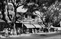 Dakar, le café Protêt. – « La place Protêt, avec son kiosque à musique et son monument aux morts en bordure du boulevard, entourée par le café Protêt, l'Eglise, le Palais de Justice (Ministère des Affaires Etrangères) et la Délégation du Cap-vert (Gouvernance) faisait face au Secrétariat Général du Gouvernement Général de I'AOF qui s'étendait jusqu'à la rue Thiers sur laquelle donnait entre autres la villa de Maître Gay, notaire, adossée au Théâtre du Palais qui allait avec ses coulisses et ses dépendances jusqu'à la rue Colbert. » (1). Le café et la place Protêt, devenue place de l’Indépendance, portent le nom du contre-amiral malouin Auguste-Léopold Protêt (1808-1862), qui fonda la ville de Dakar, après avoir pris possession de la presqu’île du Cap Vert et créé, le 25 mai 1857, un établissement français près du modeste village de pêcheurs de Dakar. Il était alors commandant des forces navales des côtes occidentales d'Afrique et commandant de l'île de Gorée, après avoir été, de 1850 à 1854, gouverneur du Sénégal. Parti servir en Extrême-Orient en 1859, il devait périr dans des combats autour de Shanghai en 1862. Le Café Protêt est un des vingt bars répertoriés à Dakar en 1948 (2) : Air Hôtel, Au bon coin, Bar de l'hôtel de ville, La Paillote, Brasserie de l'AOF, Brasserie Le Cosmos, Brasserie du Globe, Brasserie des Palmiers, Café Central, Café Dagorne, Café de Paris, Café Protêt, Chez Lucie, Excelsior bar, Hanoï, la Corvette, Le Grammont, Le Klondyke, Le Ponty, Novelty-bar, Rustict-bar, Taverne Cyrnos. Parmi ceux-ci, La Corvette, le Hanoï et Le Ponty perdurent ou existaient encore récemment. A cette époque, la ville comptait également vingt restaurants et cafés-restaurant comme Le Métropole, le Comme chez soi, Le jardin d'été,le Farid, Le Paddock, le Pavillon chinois, Le Palais, Le petit poucet, le Marie-Louise, le restaurant des Gourmets, la pension de l'Etoile, la pension Fèvre, le Thérèse, le café-restaurant de Bordeaux, le café-restaurant de l'Est, le café-restaurant de France, El Monico et l'Escale. Enfin six dancings étaient répertoriés alors : le Lido, le Jardin d'été et le Pavillon chinois, le Jockey, le Grammont et le Bodega's. Sources : (1) Diop, Birago, La plume raboutée, Paris, La Plume raboutée, Présence Africaine / Les Nouvelles Éditions Africaines, 1978. (2) Guid’AOF, Dakar, Agence Havas AOF, 1948.