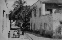 Une rue de Gorée, avant 1904. – « Grâce aux paquebots, et au commerce qui s’y développe rapidement de jour en jour, Dakar et Gorée réunies sont destinées à détrôner bientôt Saint-Louis leur métropole. Dans cinquante ans, la France peut avoir là un centre important qui monopoliserait tout le trafic de l’intérieur… […] La veille du départ, nous allâmes visiter Gorée. […] Cette petite île manque absolument de tout, même d’eau potable ; quand les citernes sont à sec, on est obligé d’en aller chercher à l’oasis de Khann ; […] Malgré l’obligation où ses habitants sont de tout tirer de la terre ferme, qui heureusement n’est qu’à quelques minutes de canot, Gorée est une station agréable et très-recherchée ; l’air y est frais et tempéré, et beaucoup de malades de Saint-Louis et de la Gambie viennent s’y rétablir. La ville occupe plus des deux tiers de la superficie totale de l’île, et les maison, construites avec vérandah et terrasses sur un seul étage, sont vastes, bien aérées, élégantes et solides » (1). – Cette carte postale fait partie du travail du célèbre photographe et éditeur dakarois Edmond Fortier (1862-1928) à qui l’on doit une somme importante de clichés sur l’Afrique de l’Ouest en général et sur le Sénégal en particulier ; il a publié en tout 3300 clichés originaux. M. Fortier tenait boutique et vivait avec ses deux filles blondes et son boy Seydou Traoré, à l’angle de la rue Dagorne et du boulevard Pinet-Laprade. Source : (1) Jacolliot, Louis, Voyage aux rives du Niger, Paris, C. Marpon et E. Flammarion, 1879.