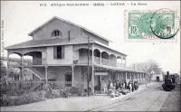 Louga, la gare. – « Louga (Sénégal) février 1885. […] N’ayant rien trouvé dans le commerce, j’entrai à la Compagnie du chemin de fer de Dakar à St-Louis, dont la construction s’achève. On m’envoya ici [à Louga], quatrième station depuis St-Louis, je ne savais rien, ni de la compagnie, ni des règlements ni du télégraphe. Je me suis acharné sur le « Bréguet » et je puis tout de même recevoir et passer une dépêche, pourvu que mes voisins n’aillent pas trop vite. La gare est une construction en bois et briques : un bureau, une chambre à coucher, une salle à manger et une cuisine. J’ai des appointements superbes : 200 francs par mois. […] Près de la gare, un village s’est créé depuis peu : de simples cases de paille, habitées par des commerçants indigènes, des traitants comme on les appelle, car le commerce des arachides se nomme la traite. La plupart de ces traitants sont convenables, et l’un d’eux, nommé Cambel, Ouolof de St-Louis, discret et bien élevé, vient souvent causer avec moi. […] Les voyageurs européens profitent de l’arrêt du train pour venir se rafraîchir ; ils savent qu’il y a dans la salle à manger une gargoulette pleine d’eau fraîche, avec un peu d’absinthe. Le train venant de St-Louis passe à 9 heures du matin et revient à 3 heures du soir ». Source : Correspondance d’Albert Nebout (1862-1940), rassemblée et publiée dans Nebout, Albert, Passions Africaines, Genève, Editions Eboris, 1995. - Cette carte postale fait partie du travail du célèbre photographe et éditeur dakarois Edmond Fortier (1862-1928) à qui l’on doit une somme importante de clichés sur l’Afrique de l’Ouest en général et sur le Sénégal en particulier ; il a publié en tout 3300 clichés originaux. M. Fortier tenait boutique et vivait avec ses deux filles blondes et son boy Seydou Traoré, à l’angle de la rue Dagorne et du boulevard Pinet-Laprade. – Quoique contemporains, ils sont nés tous deux en 1862, Albert Nebout et Edmond Fortier ne se sont vraisemblablement jamais rencontrés, le premier ayant connu le Sénégal entre 1882 et 1890, et le second étant arrivé à Dakar en 1900.