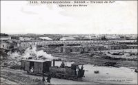 Dakar, travaux du port, chantier des blocs. – La ville de Dakar, devenue en 1902 la capitale de l’AOF, reçoit dès lors de forts investissements publics, pour développer les infrastructures tant civiles que militaires. Progressivement, le port qui est desservi par le chemin de fer à partir de1883, s’impose devant les autres installations du pays, et notamment Rufisque et Saint Louis. La machine à la manœuvre est la locomotive n°2 de type 030 T, fabriquée par les ateliers des Batignolles à Paris en 1883. – Cette photo fait partie du travail du célèbre photographe et éditeur dakarois Edmond Fortier (1862-1928) à qui l’on doit une somme importante de clichés sur l’Afrique de l’Ouest en général et sur le Sénégal en particulier ; il a publié en tout 3300 clichés originaux. M. Fortier tenait boutique et vivait avec ses deux filles blondes et son boy Seydou Traoré, à l’angle de la rue Dagorne et du boulevard Pinet-Laprade.