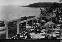 Dakar, la Pergola - écrite en 1950 - Situé sur la route de la Corniche, comme Le Lido que l'on aperçoit au fond, l'établissement La Pergola est un des vingt restaurants et cafés-restaurant que compte Dakar en 1948, comme Le Métropole, le Comme chez soi, Le jardin d'été,le Farid, Le Paddock, le Pavillon chinois, Le Palais, Le petit poucet, le Marie-Louise, le restaurant des Gourmets, la pension de l'Etoile, la pension Fèvre, le Thérèse, le café-restaurant de Bordeaux, le café-restaurant de l'Est, le café-restaurant de France, El Monico et l'Escale. Certains font également partie des six 