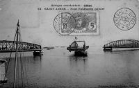 Saint-Louis, pont Faidherbe ouvert – Inauguré par deux fois, le 14 juillet 1897 par le gouverneur-général Chaudié et le 19 octobre de la même année par André Lebon, premier ministre des Colonies à se rendre au Sénégal, il remplace le pont flottant du même nom. Ce dernier avait été inauguré le 2 juillet 1865 par le colonel du Génie Pinet-Laprade, en remplacement du bac de Rouet ville, lui-même inauguré le 10 juin 1858 et qui permettait l’emport de 150 passagers par voyage pour 10 rotations par jour, ce qui s’avéra très vite insuffisant. Le pont flottant, composé de 40 pontons flottants en tôle de 4 t chacun, et d’un tablier de bois de 4 m de large, possédait une portière de trois pontons qui permettait un passage de 20 mètres pour les navires. La délicate manœuvre d’ouverture avait lieu une fois par jour. Ce pont, qui faisait au total 680 m avec une partie flottante de 355 m, nécessitait un entretien intensif et coûteux, mobilisant une équipe de 16 personnes pour vider quotidiennement l’eau infiltrée dans les pontons, vérifier les amarres… Il resta néanmoins en service 32 ans durant.