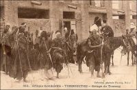 Tombouctou, groupe de Touareg. « Tombouctou s’éveille. Et pendant que les marabouts, devant le soleil levant, rappellent au peuple prosterné la grandeur d’Allah, sur le fort Bonnier monte le drapeau de la France. A ce moment, une compagnie de tirailleurs et deux pelotons de spahis sortent de la ville […] Combien reviendront de ceux qui partent ainsi à la recherche du rezzou de Touaregs signalé dans l’Est, au bord du Niger ? Les Touaregs ! guerriers légendaires, invisibles et toujours présents, survenant au galop de leurs chevaux ou de leurs méharas, tels une trombe de sable soulevée par le vent, ouragan qui passe, renverse tout et s’évanouit à l’horizon en fumée. Les Touaregs ! hommes voilés du désert, dont le litham (voile noir qui couvre le visage des Touaregs et ne laisse voir que les yeux et le nez) ajoute un mystère à celui de leur retraite » (1). Ce cliché, pris par le photographe et éditeur dakarois Edmond Fortier (1862-1928) doit dater de 1905, époque à laquelle il se rendit au Soudan et ne put, comme tous les voyageurs européens, couper à la visite de cette ville mythique aux portes du désert. Le journaliste Albert Londres, qui fit un périple en Afrique de l’Ouest en 1928 et s’y rendit à cette occasion, note pour sa part que les Européens de la colonie déconsidèrent ostensiblement cette étape ultime au nord de l’Afrique subsaharienne. « Un pèlerin qui monte à Tombouctou perd de sa valeur, à leurs yeux. Il passe pour un poète » (2).  Sources : (1) Baratier, Col., A travers l’Afrique, Paris, Arthème Fayard, 1908. (2) Londres, Albert, Terre d’ébène, Paris, Albin Michel, 1929.