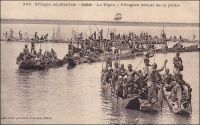 Le Niger, pirogues [au] retour de la pêche. - Jusqu’à la fin du XVIIIème siècle, les Européens se firent une idée erronée du Niger dont l’existence était mentionnée depuis l’antiquité par Pline l’Ancien (23-79). La plupart de leurs connaissances géographiques sur le continent africain reposaient, il est vrai, sur les écrits d’auteurs arabes dont le géographe Idrissi (XIIème siècle), qui n’avait jamais mis les pieds en Afrique, et le voyageur Léon l’Africain (XVIème siècle), qui décrivait plus de choses qu’il n’avait pu en voir. De fait, les occidentaux pensèrent longtemps que le fleuve prenait sa source dans le lac du Bornou, actuel Tchad, et courait vers l’ouest. Ils croyaient également qu’il aboutissait dans l’Atlantique par un immense delta pourvu de quatre branches, le Sénégal, la Gambie, le Rio Gacheo et le Rio Grande… Il fallut attendre le géographe français d’Anville, en 1749, pour imaginer que le fleuve Sénégal et le Niger étaient deux cours d’eau distincts et que le second coulait vers l’est. Et c’est l’explorateur écossais Mungo Park qui le vérifia sur le terrain en 1796, vers Ségou dans l’actuel Mali. Plus tard, la lutte pour le contrôle de cette voie navigable de l’intérieur du continent opposa colonisateurs français et britanniques. Les premiers parvinrent à tenir les sources, le delta central soudanien et le cours moyen mais se firent finalement ravir le cours inférieur par les seconds. Pour les occupants ancestraux de ces régions, le Niger est tout à la fois une véritable mer intérieure poissonneuse, un formidable couloir de communication et de commerce et la source de l’eau et du limon propices à une vaste zone fertile aux frontières du désert. - Cette carte postale fait partie du travail d’Edmond Fortier (1862-1928), photographe et éditeur établi à Dakar. Elle doit dater de fin 1905, époque à laquelle il fit un voyage au Soudan.