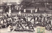 Tam-tam à Bamako. – « Deux jours de repos à Bamako, tandis que nous organisons la caravane qui doit nous emmener vert Tombouctou. […] Ce soir, encore un tam-tam : groupe d’une centaine de danseurs et d’un nombre à peu près égal de figurants. C’est une belle mascarade. Le chef des griots porte un peplum bleu-noir et est coiffé d’un casque doré de lancier Second Empire, à cimier de crin. Les vieilles femmes, comme toujours, sont  déchainées ; elles portent les couleurs les plus voyantes et ne le cèdent à personne en lascivité. La grande vedette remue furieusement le derrière ; un homme se détache du groupe, et pour mettre ce spectacle en valeur, pose une main au bon endroit ; on voit ses doigts noirs se détacher sur la jupe blanche de la danseuse. Pendant ce temps les tambours lâchent des pétarades d’obusiers qui font trembler le palais. Les femmes poussent des cris de tête, les balafons de bois sonore laissent couler des gammes sur leurs deux octaves, et les clochettes de fer attachées aux chevilles font un bruit de rideau métallique. Les acteurs se passent un seau de zinc plein d’eau, à même lequel ils boivent, sans interrompre leur action. Ils s’avancent et profèrent d’un air féroce des paroles hurlées, qu’on nous affirme encore être nos louanges et celles des parents qui nous ont conçus ; les chefs commentent cette récitation héroïque par des exclamations parlées qui en soulignent le sens, comme les méthodistes américains accompagnent d’aboiements les discours de leur ministre ; c’est tout à fait le shouting des nègres baptistes. Le proverbe guinéen dit : Les griots chantent seulement les louanges des vivants » (1). Cette carte postale fait partie du travail d’Edmond Fortier (1862-1928), photographe et éditeur établis à Dakar. Elle doit dater de fin 1905, époque à laquelle il fit un voyage au Soudan.  Sources : (1) Morand, Paul, A.O.F. de Paris à Tombouctou, Paris, Flammarion, 1928.
