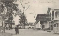 Togo : Marktplatz von Agome-Palime. - Pour édifier les bâtiments nécessaires au développement de la colonie, les architectes allemands du Togo vont se montrer créatifs. Ils ont en effet à composer avec le coût exorbitant des matériaux importés et avec des impératifs techniques inhabituels pour eux, liés aux conditions climatiques tropicales. Leurs constructions doivent en effet tout à la fois protéger leurs occupants du soleil intense, de précipitations diluviennes et de l’humidité émanant du sol. Il leur faut aussi résister aux tornades dévastatrices de la saison des pluies et durer pour s’inscrire dans le temps. Pour cela, les bâtisseurs vont mobiliser leurs connaissances architecturales européennes, faire appel à quelques pièces venues d’Allemagne, mais aussi s’inspirer des modes de construction traditionnels locaux et utiliser des matériaux disponibles sur place. Ainsi, comme le font les constructeurs de la région depuis des lustres, ils vont veiller à orienter leurs édifices d’est en ouest pour n’offrir que la faible surface des pignons aux ardeurs du soleil levant et couchant. Ils optent souvent pour des galeries, ou de larges avancés du toit, pour ombrager les longues façades. Ils utilisent les vents nord-sud dominants pour aérer, grâce à des fenêtres sur les deux façades offrant une circulation d’air intérieure de part en part. Ils recourent aussi à une technique de dite de noyau central, où la maçonnerie est protégée de l’échauffement solaire par des écrans plus légers en bois. Enfin, ils reprennent à leur compte le système de double toit isolant, avec une circulation d’air entre les deux couvertures permettant de dissiper la chaleur des tôles exposées au soleil. Au bout du compte, ces emprunts, cette hybridation des techniques et des styles, aboutissent à une « architecture tropicale allemande » originale, dont les principes pourraient figurer sans pâlir parmi ceux de la construction durable contemporaine.