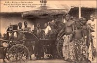 Adjiki, Roi nègre dans son carrosse au milieu de ses Ministres. – Le roi Adjiki, monte sur le trône de Porto Novo en février 1908. Il connait à cette occasion une célébrité inédite dans la presse à sensation française. Cet engouement tient peut être au fait qu’il est le fils et le successeur du roi Toffa - l’allié de la France contre le roi Béhanzin d’Abomey à la fin du XIXème siècle – ou à la nostalgie hexagonale pour les choses de la royauté. Ou encore au passage au Dahomey du grand photographe dakarois Edmond Fortier, accompagnant la visite officielle du ministre des colonies en Afrique de l’Ouest de 1908, depuis son escale sénégalaise. C’est d’ailleurs lui l’auteur de ce cliché joliment composé. Le  Couronnement d’Adjiki est rapporté par Le Petit Journal Illustré, dans son édition du 5 avril 1908 : « Le prince Adjiki, fils de Toffa, coiffé du bicorne à plumes blanches, insigne de la souveraineté, assiste aux fêtes de son couronnement. Nous donnons plus loin, dans notre « variété », de curieux et pittoresques détails sur la façon dont on célébrait jadis, et dont on célèbre aujourd’hui, l’avènement d’un nouveau souverain dans ces contrées de la côte des Esclaves qui sont à présent colonies françaises. C’est le récent décès de Toffa, roi de Porto-Novo, et le couronnement de son fils, le prince Adjiki, qui nous ont fourni l’occasion de donner à nos lecteurs, d’après des documents d’une absolue exactitude, cette intéressante gravure sur les fêtes qui se sont déroulées à Porto-Novo. Adjiki a reçu le bicorne à plumes blanches, insigne du pouvoir, des mains de M. Marchal, lieutenant gouverneur de la colonie française du Dahomey, en même temps qu’un arrêté le nommait « chef supérieur des territoires français du Bénin ». De ce fait, Adjiki a pour attribution le concours à l’exécution de toutes les mesures prescrites par le lieutenant gouverneur ou par le président de Porto-Novo. Il intervient notamment lorsqu’il en est requis, auprès des chefs de région, de village ou de quartier pour les maintenir dans l’obéissance totale en toutes circonstances ou pour y maintenir les habitants du cercle de Porto-Novo. Il remplit les fonctions judiciaires qui peuvent ou pourront lui être dévolues par les actes régissant la matière. Le prince Adjiki reçoit, en cette qualité de chef supérieur un traitement annuel de 25.000 francs, outre la part lui revenant des remises sur l’impôt personnel, allouées aux chefs indigènes par les règlements en vigueurs. Et voilà comment il arrive parfois que la République fait des rois ».