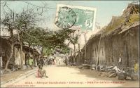 Porto-Novo, une rue. – « Porto-Novo et la banlieue d’Hogbonou nous offrent des types d’habitations retrouvés nulle part ailleurs. Rien n’est plus curieux que de pérégriner le long des ruelles étroites, creusées de ravines, coupées de ponts fragiles. Nous voyons des maisons dont la terre de barre est dissimulée sous un revêtement de couleur bleu pâle, ocre jaune, rouge, garnies de mirador, de faux balconnets, de croisillons aux fenêtres, vestiges des premiers Portugais qui vinrent sur cette Côte des Esclaves, vers le XVIè siècle » (1). Cette carte postale fait partie du travail du photographe et éditeur dakarois Edmond Fortier (1862-1928). Elle appartient à un reportage qu’il mena dans le sud du Dahomey en 1908, alors qu’il accompagnait, depuis l’escale de Dakar, le voyage officiel accompli sur la côte oust africaine par le Ministre des colonies Raphaël Milliès-Lacroix. Sources : (1) Bonzon, L., Despois, J., Lacharriere de, L., Leyritz, A., Marquis-Sebie, D., Multedo de, C., Rectenwald G. et Reste, J.F., Le domaine colonial français, Paris, éditions du Cygne, 1929.