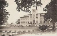 Lomé, le Palais du Gouverneur. - Construit de 1898 à 1905, il abritait au rez-de-chaussée les bureaux et à l’étage les appartements du gouverneur, selon le modèle habituel des bâtiments coloniaux. Le gouverneur August Kohler (1858 – 1902), qui était au Togo depuis 1895, décida en 1898 l’emplacement à 250 m de la plage. Pour que l’ensemble de l’édifice puisse être vu depuis les navires en mer, et ce malgré un talus qui bordait le rivage, il reçu un sous-bassement de 3,50 m. Sur ce cliché, on distingue, au mat de drapeau du bâtiment, les couleurs françaises. L’édifice devait continuer en effet à abriter l’exécutif du Togo, durant l’occupation britannique, entre 1914 et 1920, puis sous le mandat français et même après l’indépendance, jusqu’à la construction de la nouvelle présidence, sur un terrain mitoyen, en 1970. Le journaliste Jean Martet raconte ainsi sa visite au Palais en 1933, à l’époque le gouverneur qui représente Paris dans ce territoire confié à la France par la SDN est Robert de Guise (dans cette fonction entre 1931 et 1933) : « Le bureau de M. de Guise est au rez-de-chaussée de cette grande construction vaguement moyenâgeuse qui a été bâtie par les Allemands face à la mer et qu’on appelle, pompeusement, le Palais du Gouvernement. Les appartements du gouverneur sont au premier : de grandes pièces, claires et fraiches, avec vue sur cette mer sans une voile, sans une fumée, et les mendiants du parc, les palmiers de la belle et large route qui borde la plage. Nous trouvâmes Mme de Guise comme elle était en train de donner des ordres à son chauffeur, lequel est prénommé Momo. Momo est un noir vêtu de blanc, avec, à la main, une belle casquette, Mme de Guise est une femme souriante et charmante. Elle vint à moi et me dit : - Il y a par ici une ville qui s’appelle Palimé. Palimé a élu l’année dernière sa plus belle négresse, Miss Palimé. Momo est passé par là et a enlevé Miss Palimé. J’aime beaucoup Momo. Je m’assis. C’était un grand salon avec de jolis meubles de bois clair, et, par terre, des tapis de fourrure, quatre tapis de fourrure » (1). Sources : (1)  Martet, Jean, Les bâtisseurs de royaumes, Paris, Albin Michel, 1934.