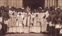 L’église en marche : une ordination à Ouidah. Carte postale des Missions Africaines de Lyon. – L’évangélisation du Dahomey, dans la deuxième moitié du XIXème siècle, est une gageure pour les missionnaires catholiques. Ils considèrent en effet cette contrée comme particulièrement sauvage en raison de la persistance des sacrifices humains. « L’auréole de barbarie qui couronnait si lugubrement le nom du Dahomey exerçait une sorte de fascination », raconte Valérien Groffier (1), secrétaire général de l’œuvre de la propagation de la foi à Lyon, pour expliquer l’insistance des hommes d’église à s’y rendre. Le récit des hécatombes, accompagnant les funérailles du roi Ghézo en 1858 et la « fête des Coutumes » à Abomey en 1860 – rapporté par M. Lartigues agent local des factoreries Régis de Marseille-, qui auraient coûté la vie à 3000 personnes chacune, décidèrent Rome à envoyer les pères des Missions Africaines de Lyon. Le pape Pie IX accepta le projet en 1860 et les premiers missionnaires débarquèrent à Ouidah en avril 1861. Usant de symbolique, son successeur, Benoit XVI, a choisi cette ville pour lancer cent cinquante ans plus tard un appel à l’Afrique. C’est la troisième visite pontificale dans le pays –Jean-Paul II y est venu en 1982 et 1993- et cela marque l’importance croissante du continent noir dans l’église contemporaine. Les ordres missionnaires comptent souvent de nos jours plus de membres originaires d’Afrique que d’Europe. Et l’avenir démographique de cette religion semble devoir, pour partie, se jouer au sud du Sahara. Sources : (1) Groffier, V., Héros trop oubliés de notre épopée coloniale, Lyon-Paris, Librairie catholique Emmanuel Vitte, 1928.