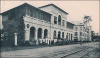 Lomé, l’hôtel Gariglio. – Situé au centre historique de la ville, dans la rue du Commerce – l’ancienne Hamburgerstrasse de l’époque allemande –, l’établissement est devenu par la suite l’hôtel du Golfe. Sous ce nom, Il accueillait encore très récemment les voyageurs préférant son charme un peu suranné à l’ambiance standardisée des hôtels modernes de la place. Dans l’entre deux guerres, il connut une certaine ambition culturelle, puisqu’il recevait les séances de cinéma avant la création de salles dédiées au septième art dans la capitale togolaise. La taille restreinte des lieux et son implantation dans le quartier européen réservaient ces projections à un public de privilégiés. Un peu plus tard, en 1941, l’hôtel est explicitement mentionné dans l’enquête menée par les autorités militaires françaises de Lomé pour élucider la fuite de deux matelots de l’aviso La Gazelle vers la colonie britannique voisine de Gold Coast. Sur ce cliché, on distingue, à côté de l’hôtel, le bâtiment caractéristique abritant la succursale locale la maison de commerce John Holt de Liverpool.