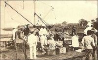 Appontement de Porto-Novo. Avez-vous quelque chose à déclarer ? – Il s’agit vraisemblablement du débarcadère gouvernemental de Porto-Novo, situé sur la lagune à l’ouest des installations portuaires commerciales et relié au Palais du gouverneur par l’avenue William Ponty. Ce type d’ouvrage était courant dans la ville, car la lagune constitua longtemps l’unique voie de communication. Aussi, l’activité commerciale se développa autour de ce cordon qui mène vers Cotonou, où étaient organisées les rades foraines permettant de charger et décharger les navires et où fut ensuite édifié un wharf. Les maisons de commerce européennes, arrivées dans la ville avant et après le traité de protectorat français de 1863, installèrent chacune leur propre appontement sur la lagune, pour assurer le trafic des marchandises importées et exportées. Parfois même, des petits canaux, appelés body et accessibles aux embarcations, furent creusés pour s’approcher de la lagune. Les abords de la lagune étant trop marécageux pour bâtir des installations solides, les  négociants s’implantèrent autour du marché traditionnel, en ménageant des chemins de portage et roulage sur talus pour rallier leurs appontements. – Le commentaire humoristique de cette carte postale, « avez-vous quelque chose à déclarer ? », fait malicieusement allusion aux droits de douanes, qui furent un enjeu décisif dans les politiques coloniales de cette région très disputée par les commerçants européens et africains.