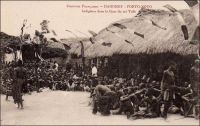 Porto-Novo, Indigènes dans la Cour du roi Toffa. – Dix-neuvième souverain de la dynastie des princes Allada à exercer le pouvoir sur le royaume de Porto-Novo, Toffa eut également le plus long règne : monté sur le trône en 1874, il y demeura jusqu'à sa mort en 1908. Signataire d’un traité d’amitié et de protectorat avec la France en 1883, il laisse une image controversée dans l’histoire dahoméenne : c’est pour le protéger des attaques du royaume d’Abomey – et pour défendre leurs intérêts territoriaux et commerciaux - que les Français ménèrent la campagne militaire de 1892, aboutissant à la destitution et au bannissement du jeune roi Béhanzin d’Abomey.