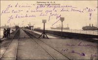 Wharf et rade de Cotonou. – Appelé à soutenir la vocation portuaire de la ville et à faciliter le débarquement des troupes alors que la guerre se profile – en 1892 -, le wharf de Cotonou est construit entre 1891 et 1893. Long de 300 mètres, il ouvre au trafic commercial le7 mai 1893. Au départ, il ne permet aux navires d’accoster qu’au rythme d’un par mois. Insuffisant pour absorber tout le trafic de fret et de passagers du Dahomey - hormis celui avec Lagos qui passe par voie fluviale sur la lagune et le cabotage local résiduel au port de Grand Popo sur l’embouchure du Mono -, il est remplacé en 1928 par un édifice plus important (400 mètres) et mieux équipé. Les navires sont chargés et déchargés directement au mouillage en rade foraine, à un kilomètre du wharf, grâce à une flottille de 26 baleinières de 15 à 25 tonnes et de 8 remorqueurs de 60 à 75 chevaux. Treize grues électriques, d’une capacité de levage allant de 10 à 20 tonnes, permettent de transborder les charges des baleinières sur le wharf où le transport est relayé par voie ferrée. Aussi utile qu’il soit, ce dispositif montre bientôt ses limites. Les moyens relativement modestes et les manipulations complexes qu’ils supposent occasionnent des pertes importantes dans les cargaisons : les coûts sont trois fois plus élevés qu’au port de Dakar. De plus, ces équipements ne permettent guère de traiter plus de 1000 tonnes par jour et, compte tenu des avaries, la capacité annuelle plafonne à 300 000 tonnes. Enfin en période de pointe, les délais se prolongent, provoquant un inconfort certain pour les passagers qui attendent d’être débarqués par le fameux panier. En 1964, la capitale du Dahomey se dote d’un port en eau profonde, remplaçant définitivement le wharf et le système de rade foraine devenus obsolètes. – Cette carte, éditée sous la signature « Collection Géo Wolber, Dahomey », est une curiosité. Elle fait partie des séries produites et diffusées après la première guerre mondiale – et jusqu’en 1937 - par les repreneurs de la société allemande Wölber, mise sous séquestre par les autorités coloniales françaises dès le début des hostilités. - Le courrier « Asie », mentionné manuellement par l’expéditeur de cette carte postale, a connu un destin des plus chaotique. Entré en service en 1914, il est utilisé comme navire hôpital et transport de troupes pendant la première guerre mondiale, avant de faire les lignes de la côte africaine pour la compagnie des Chargeurs Réunis. Il connaît plusieurs avaries, accidents, échouages et incendies : en sortant de la Gironde en 1920, dans le port de Dakar en 1925, près de Matadi (Congo) en 1927… Il est saisi par l’armée italienne en 1942, par les Allemands en 1943 qui le remettent aux Italiens pour lesquels il navigue sous le nom de « Rossano » avant d’être coulé en 1944 par un bombardement allié dans le port de Gênes. Renfloué, il finit sa carrière en chavirant dans le port après incendie…