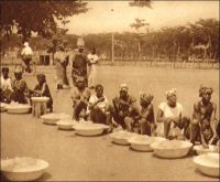 Lomé, vendeuses au marché, (vers 1925). – Dès l’époque coloniale allemande, les revendeuses, éléments caractéristiques du commerce de détail au Togo, commencent leurs fructueuses pratiques, aux côtés de grandes maisons de commerce comme Deusche Togo Geselischaft, Boedecker et Mayer, J. K. Victor, Goedel, et de quelques marchands syriens. Des fortunes accumulées sur la base de petits commerces feront, de quelques togolaises particulièrement avisées en affaires, des « Mama-benz », figures éclatantes de la réussite économique.