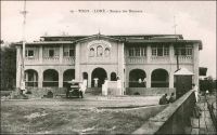 Lomé, Bureau des Douanes. – Ce bâtiment, construit en 1903 par les Allemands juste en face du wharf, a été démoli en 1983, laissant place à un centre commercial moderne comptant des salles de cinéma, un casino, une boite de nuit et un hôtel. Les douanes jouaient un rôle capital dans le dispositif colonial allemand. Elles fournissaient en effet la majeure partie des ressources budgétaires du Togo, qui finit par ne plus rien coûter à la métropole à partir de 1906. Les Allemands considéraient de ce fait le Togo comme « Musterkolonie », la colonie modèle. Les marchandises pour tout le territoire, qui devaient être obligatoirement débarquées par le wharf -et donc directement devant la douane-, étaient soumises à une taxe de 10%. Seuls certains articles, comme les sacs, les bouteilles ou les wagons, bénéficiaient d’une franchise douanière. Les Anglais et les Français qui succèdent aux Allemands après la défaite locale de 1914, maintiennent dans un premier temps un système douanier comparable à celui de leurs prédécesseurs. Ensuite, tandis que les Anglais adoptent le même régime douanier au Togo britannique qu’en Gold Coast, les Français instaurent au Togo sous mandat un statut moins favorable qu’au Dahomey et créent ce faisant une concurrence entre les deux territoires mitoyens qui obligea à rétablir un poste de douane à Aného et un contrôle de la frontière sur le Mono. Progressivement, la situation est normalisée, et peu avant la seconde guerre mondiale le régime douanier des deux territoires est aligné sur celui du reste de l’AOF. - La photo est prise depuis le wharf construit par les Allemands, dont on aperçois une partie de la rambarde à droite de l'image. Cette carte postale a été éditée par Alex Accolatse. Ce notable loméen
