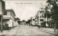 Lomé, la rue du Commerce. – La plus ancienne rue commerciale de Lomé, appelée Hamburgerstrasse du temps de la colonie allemande, regroupait la plupart des factoreries de la place, et le siège local des compagnies maritimes et de négoce. On y trouvait notamment, aux côtés du temple et de la librairie évangélique, la firme Bödecker-&-Meyer,  les bureaux de l’armateur allemand Woerrmann, devenus ministère du commerce dans les années 1970. S’y trouvait aussi l’hôtel  Vogt, qui partageait le marché avec l’hôtel Kaiserhoff. Un peu plus tard, ils cédèrent la place à l’Hôtel du Golfe. Celui-ci est explicitement mentionné en 1941, dans l’enquête menée par les autorités militaires françaises de Lomé pour éclaircir le passage vers la colonie britannique voisine de la Gold Coast, de deux matelots de l’aviso La Gazelle. - Alex Accolatse, à qui l’on doit ce cliché, avait commencé sa carrière de photographe à la toute fin du XIXème siècle en Gold Coast. Il vint s’installer en 1900 à Lomé, où il exerça jusqu’en 1956 et s’éteignit en 1975 à 95 ans.